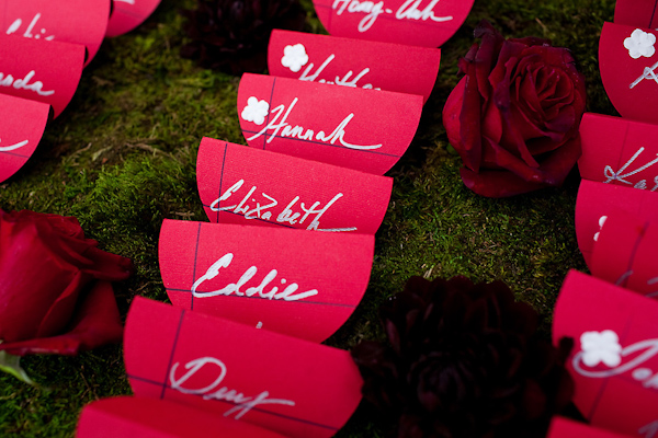 Red seating cards with silver ink displayed on green grass with red roses - wedding photo by Michael Norwood Photography